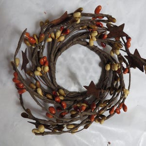 May include: A circular wreath with brown twigs, adorned with orange, cream, and brown berry clusters. Rusty brown star-shaped accents are interspersed throughout the wreath, creating a rustic, autumnal aesthetic. Perfect for seasonal home decor.