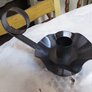 May include: Black metal candle holder with a curved arm and a fluted base. The holder is designed to hold a single candle.