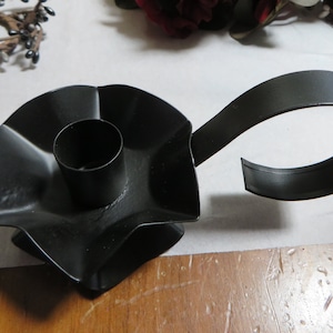 May include: Black metal candle holder with a star-shaped base and a curved handle. The holder is designed to hold a standard-sized candle.