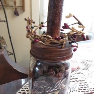 May include: A glass jar with a rusty metal lid filled with dried berries. The jar is decorated with a brown, white, and red berry garland.