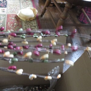 May include: Decorative branches with small, colorful accents. The branches feature a mix of burgundy, green, and cream-colored beads. The branches are arranged in a cardboard box, suggesting they are new.