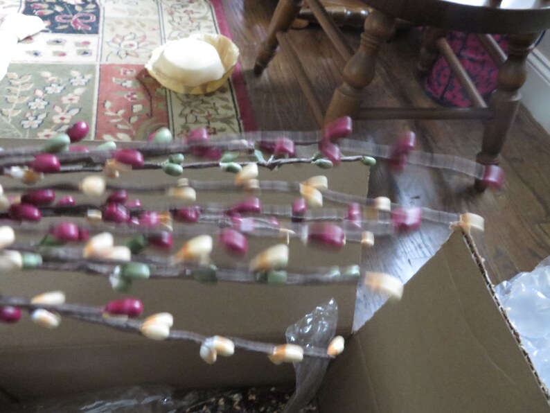 May include: Decorative branches with small, colorful accents. The branches feature a mix of burgundy, green, and cream-colored beads. The branches are arranged in a cardboard box, suggesting they are new.