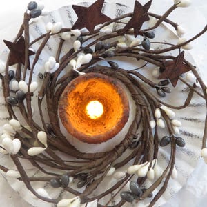 May include: A rustic twig wreath with white and gray berries, decorated with rusty metal stars and a lit candle in the center.