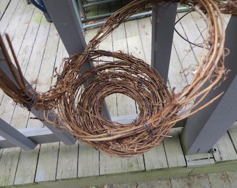 May include: A natural grapevine wreath, featuring a circular design with a central opening. The wreath is made of intertwined brown vines, creating a rustic and organic aesthetic. Ideal for home decor or seasonal crafting.