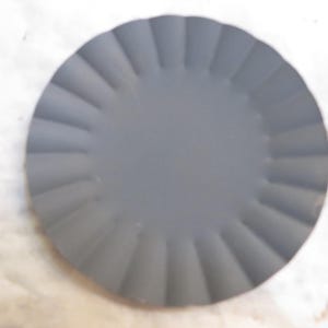 May include: A round, gray plate with a scalloped edge. The plate has a matte finish and a simple, elegant design. The plate is suitable for serving appetizers or desserts.
