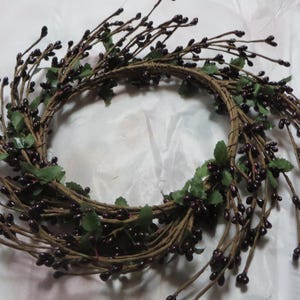 May include: A brown twig wreath with dark purple berries and green leaves.