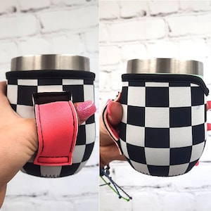Puede incluir: Un portavasos de neopreno a cuadros blanco y negro con un agujero para el pulgar rosa. El portavasos está diseñado para adaptarse a un vaso de tamaño estándar.