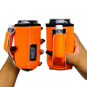 May include: Orange neoprene can cooler with a black strap and a small pocket for a lip balm or vape pen. The cooler has the text "HANDLER" and "@LITTHANDLERS" printed on it.