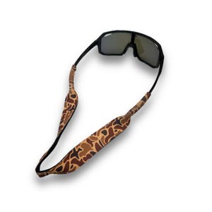May include: Black sunglasses with a camouflage patterned strap. The strap is made of a soft, flexible material and is designed to keep the sunglasses securely in place.