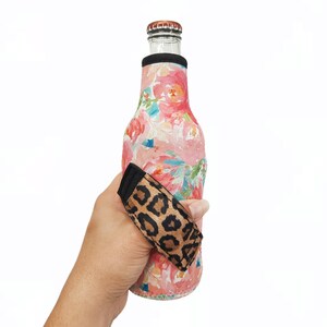 May include: A pink and blue floral patterned neoprene bottle cooler with a black and brown leopard print strap.