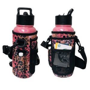 Puede incluir: Botella de agua rosa con una funda aislante de estampado de leopardo y una correa de transporte negra. La funda tiene un bolsillo de malla y un bolsillo pequeño para bálsamo labial.
