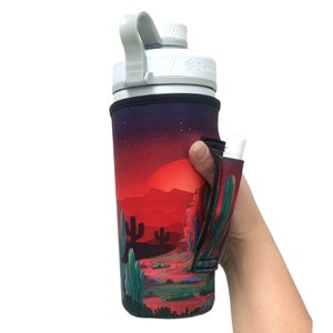 May include: A white water bottle with a black and red desert scene design. The bottle has a black carrying strap and a white lid. The bottle is in a hand.