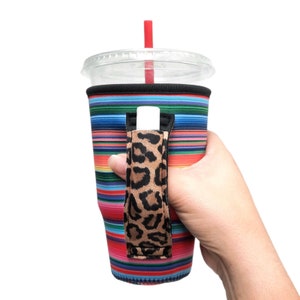 May include: A colorful striped neoprene cup holder with a leopard print handle. The holder is designed to fit a standard-sized cup and has a slot for a straw.