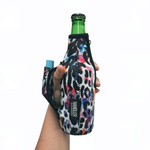 May include: A black and white leopard print bottle holder with pink, blue, and orange accents. The holder has a strap for carrying and the text "HANDLER @LITHANDLERS" is printed on the side.