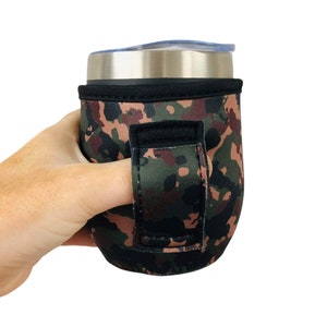 Puede incluir: Un portavasos de neopreno con estampado de camuflaje y asa negra. El portavasos está diseñado para adaptarse a un vaso de tamaño estándar y tiene un bucle para el dedo para facilitar su transporte.