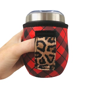 Puede incluir: Portavasos aislante de tela roja y negra a cuadros con un asa de estampado de leopardo. El portavasos está diseñado para adaptarse a un vaso de tamaño estándar.