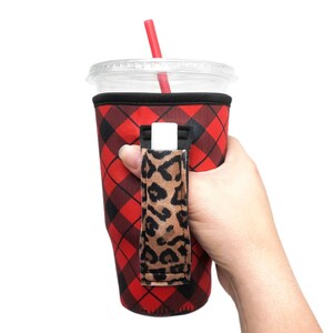 May include: Red and black plaid insulated cup holder with a leopard print handle. The holder is designed to fit a standard-sized cup and has a built-in straw holder.