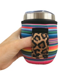 Puede incluir: Un portavasos de neopreno a rayas de colores con un asa de estampado de leopardo. El portavasos está diseñado para adaptarse a un vaso de tamaño estándar.