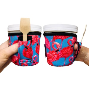 May include: Two insulated beverage holders with a flamingo print. The holders are blue with pink flamingos. One holder has a wooden spoon sticking out of the top.