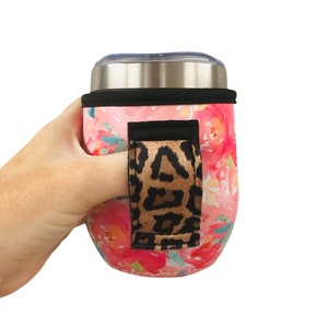Puede incluir: Portavasos de neopreno con estampado floral rosa y blanco con una correa para el dedo de estampado de leopardo negro y marrón.