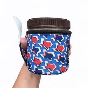 May include: A blue and red neoprene insulated cup holder with a Texas state outline pattern. The holder has a black strap and a white spoon attached to it. The text "HANDMADE" is visible on the side of the holder.