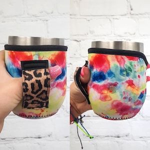 Puede incluir: Un enfriador de latas de neopreno de color tie-dye con un asa de estampado de leopardo. El enfriador está diseñado para adaptarse a una lata o botella estándar de 350 ml.