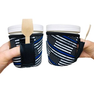 May include: Two black and white insulated cup holders with a blue line American flag design. Each holder has a black strap and a slot for a spoon.