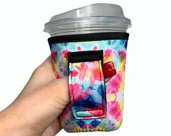 May include: A colorful tie-dye neoprene cup holder with a black strap handle. The holder is designed to fit a standard size to-go cup.