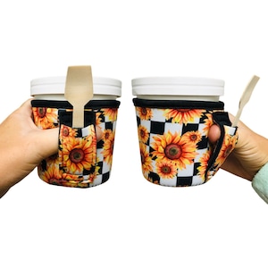 May include: Two white cups with black and white checkered and sunflower print insulated cup holders. The holders have a slot for a spoon or straw. One cup holder has a wooden spoon in the slot.