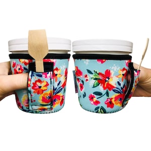 May include: Two white cups with black rims and floral print insulated sleeves. The sleeves have a finger hole and a slot for a spoon. The spoons are made of wood.