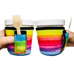 May include: Two rainbow striped insulated cup holders with a built-in spoon holder. Each holder has a black strap handle and a yellow accent.