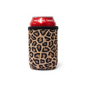 Puede incluir: Un enfriador de latas de neopreno con estampado de leopardo con una lata roja en su interior. La lata tiene el texto "ORIGINAL TASTE" impreso en ella.