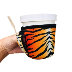 Puede incluir: Portavasos de neopreno con estampado de tigre naranja y negro con un agujero para el dedo y una ranura para una cuchara. El portavasos está diseñado para adaptarse a una taza de tamaño estándar.