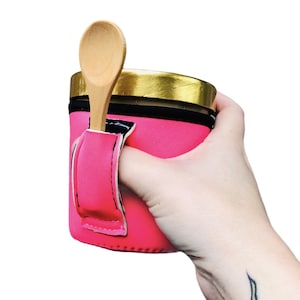 May include: Pink insulated cup holder with a black strap and a wooden spoon sticking out of the top. The cup holder is designed to keep ice cream cold and prevent melting.