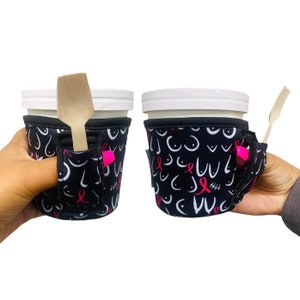 Puede incluir: Dos portavasos aislados en blanco y negro con una cinta rosa y un diseño de concienciación sobre el cáncer de mama. Los portavasos tienen una ranura para una cuchara o una pajita.