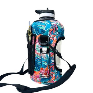 Puede incluir: Una botella de agua transparente con una correa negra y una funda de neopreno con estampado tropical. La funda tiene un bolsillo para un teléfono u otros artículos pequeños.