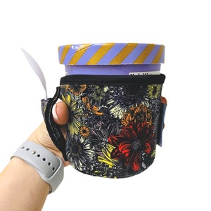 May include: A black and white floral print insulated cup holder with a purple and gold striped ice cream container inside.