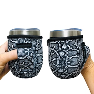 Puede incluir: Dos portavasos de neopreno con estampado de piel de serpiente en blanco y negro con un agujero para el dedo para facilitar su transporte. Los portavasos están diseñados para adaptarse a un vaso de tamaño estándar.