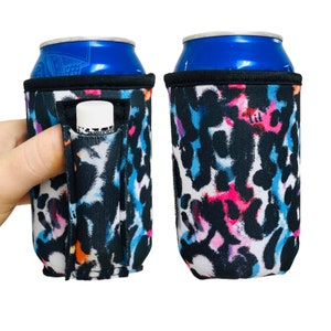 May include: Two black and white neoprene can coolers with a colorful abstract print. One cooler has a slot for a lip balm or small tube.