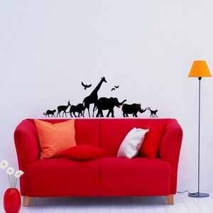 Puede incluir: Un sof&aacute; rojo con dos almohadas se encuentra frente a una pared blanca con una silueta negra de una jirafa, un elefante, un rinoceronte y otros animales. Una l&aacute;mpara amarilla est&aacute; en la esquina de la habitaci&oacute;n.
