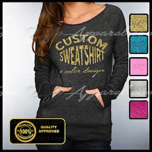May include: A dark gray sweatshirt with a gold glitter design that says "CUSTOM SWEATSHIRT + color design". The sweatshirt has a pocket on the front and a tag that says "QUALITY APPROVED 100% GUARANTEED".