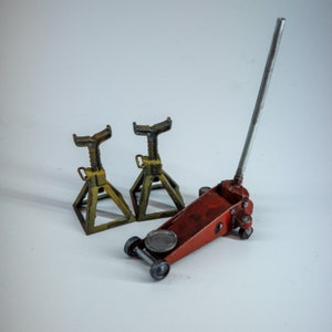 May include: A red hydraulic floor jack with a silver handle and two yellow and brown jack stands. The jack stands are made of metal and have a triangular base. The jack is on wheels.