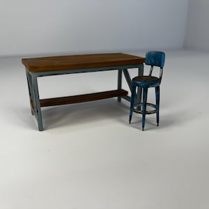 May include: A miniature wooden table with a brown top and gray legs, and a matching blue stool. The table has a lower shelf and the stool has a round seat and backrest. The furniture has a distressed, vintage appearance.