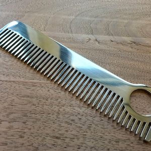 May include: A silver metal comb with a rounded handle and a hole in the handle. The comb has fine teeth.