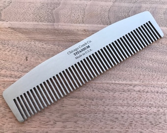 Puede incluir: Un peine de titanio plateado con el texto "Chicago Comb Co. TITANIUM Made in U.S.A." en la parte posterior.