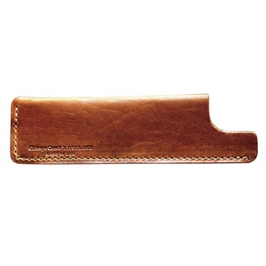 Könnte beinhalten: Ein braunes Lederetui für einen Kamm mit dem geprägten Text "Chicago Comb x Ashland Made in USA" auf der Vorderseite.