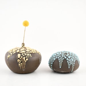 May include: Two ceramic vases with a crackled glaze finish. One vase is brown with a yellow glaze and the other is brown with a blue glaze. Both vases are round and have a textured surface.