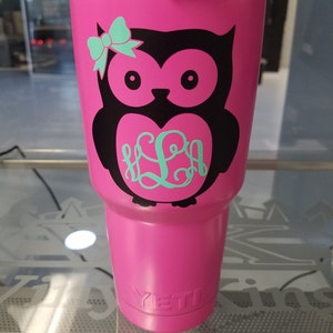 Puede incluir: Un vaso Yeti rosa con un diseño de búho negro y un monograma turquesa en forma de corazón. El búho tiene un lazo turquesa en la cabeza.