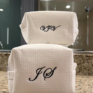 May include: Two white waffle-weave zippered pouches with black embroidered initials. The top pouch has the initials "VJV" and the bottom pouch has the initials "JS".