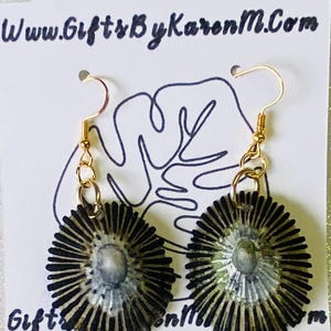May include: A pair of handmade earrings with gold-colored hooks and circular pendants. The pendants feature a radial design in black and gray, with a central, lighter-colored oval. The earrings are displayed on a white card with the text "www.GiftsByKarenM.com".
